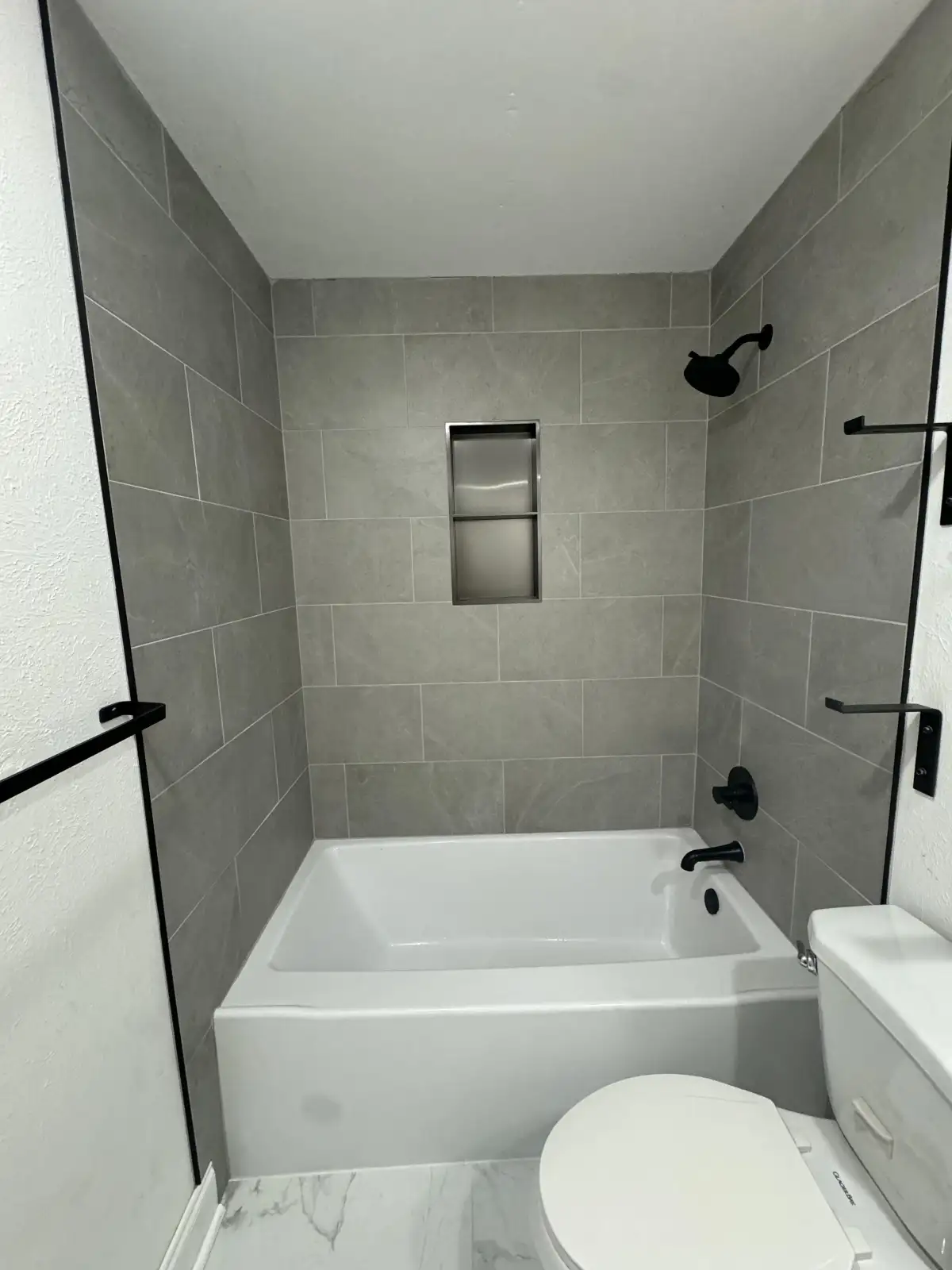 Clean modern tiled tub surround with black fixtures and recessed niche