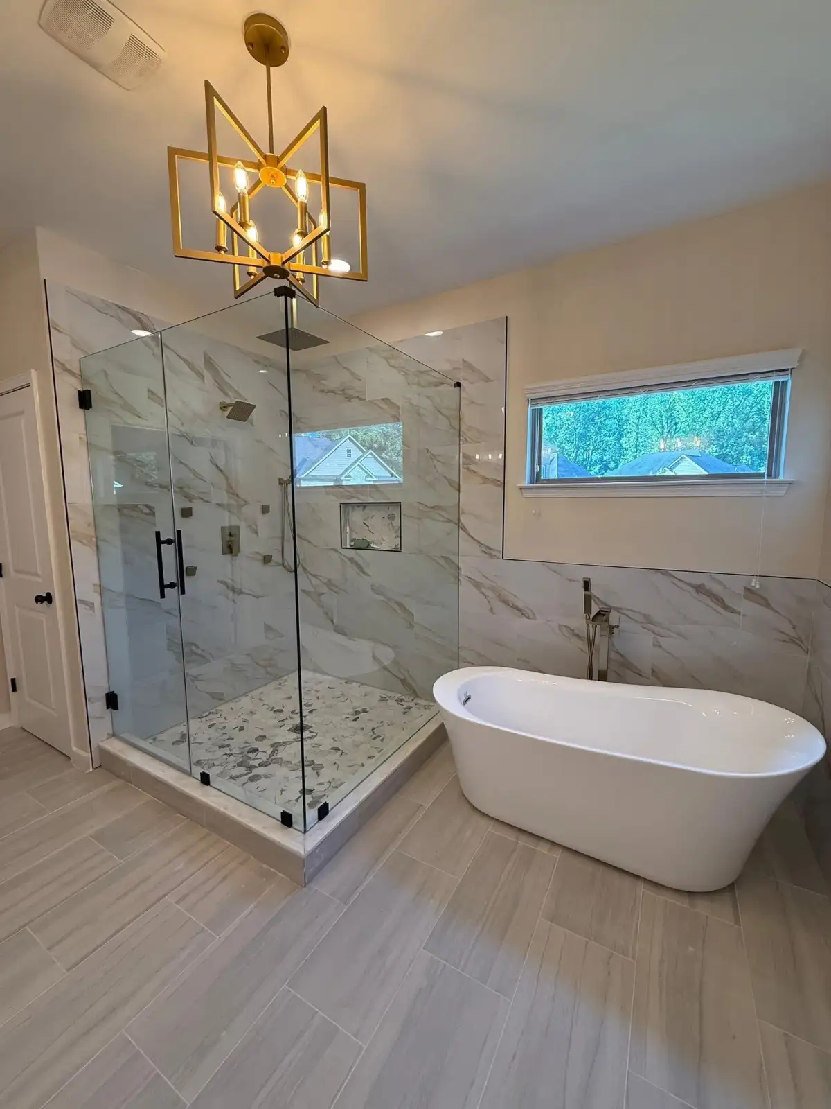 Luxury bathroom remodeling with frameless glass shower, freestanding tub, marble finishes, and gold chandelier in Fort Worth