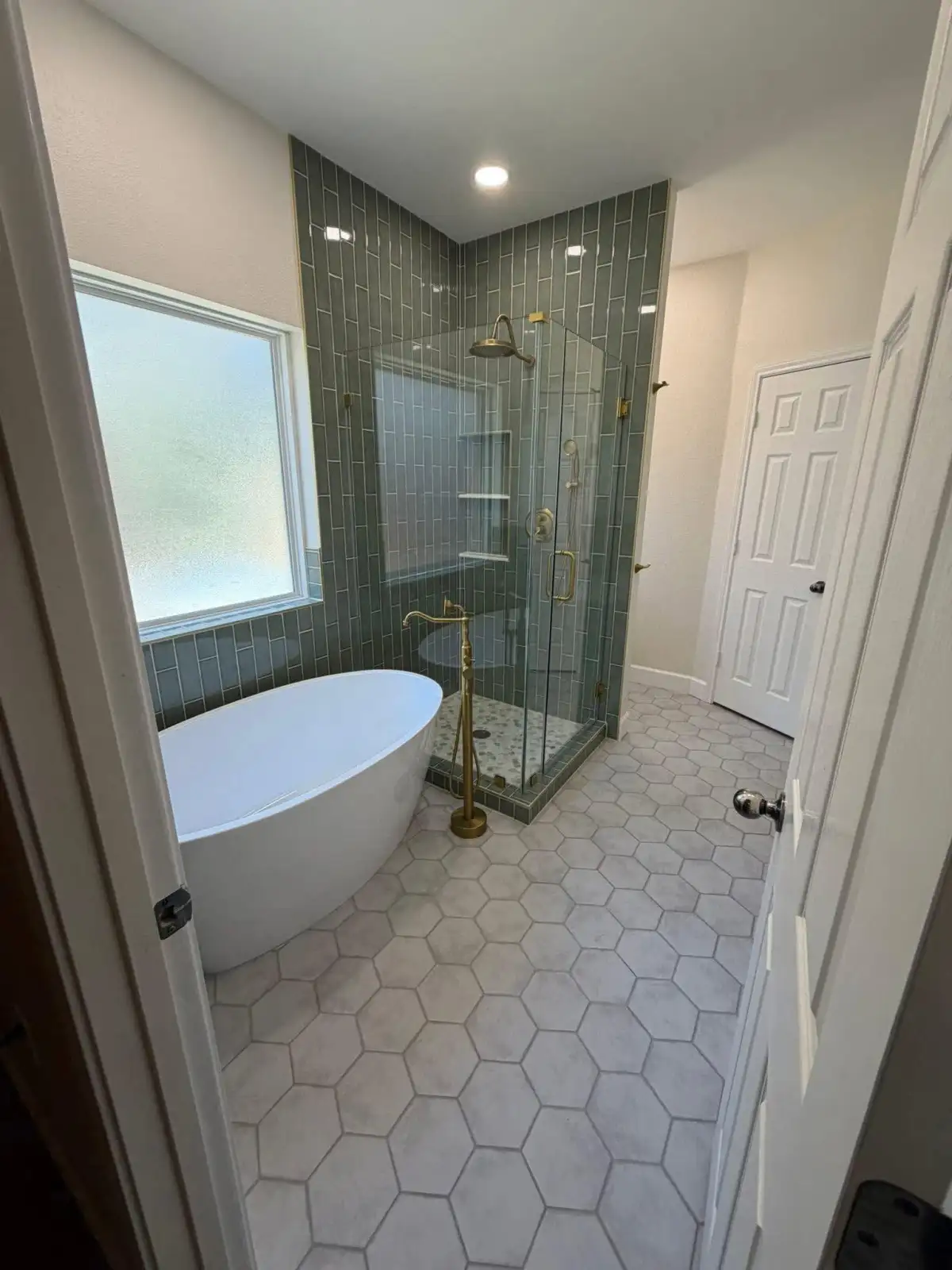 Bathroom with freestanding tub, green tile shower, hexagon floor tile, and gold fixtures