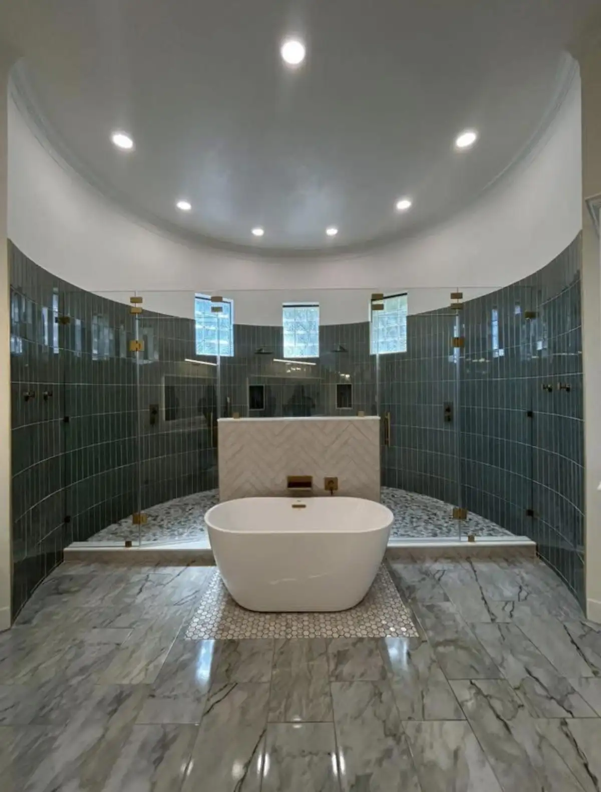 Curved luxury bathroom with freestanding tub, blue-green tile accents, and marble finishes