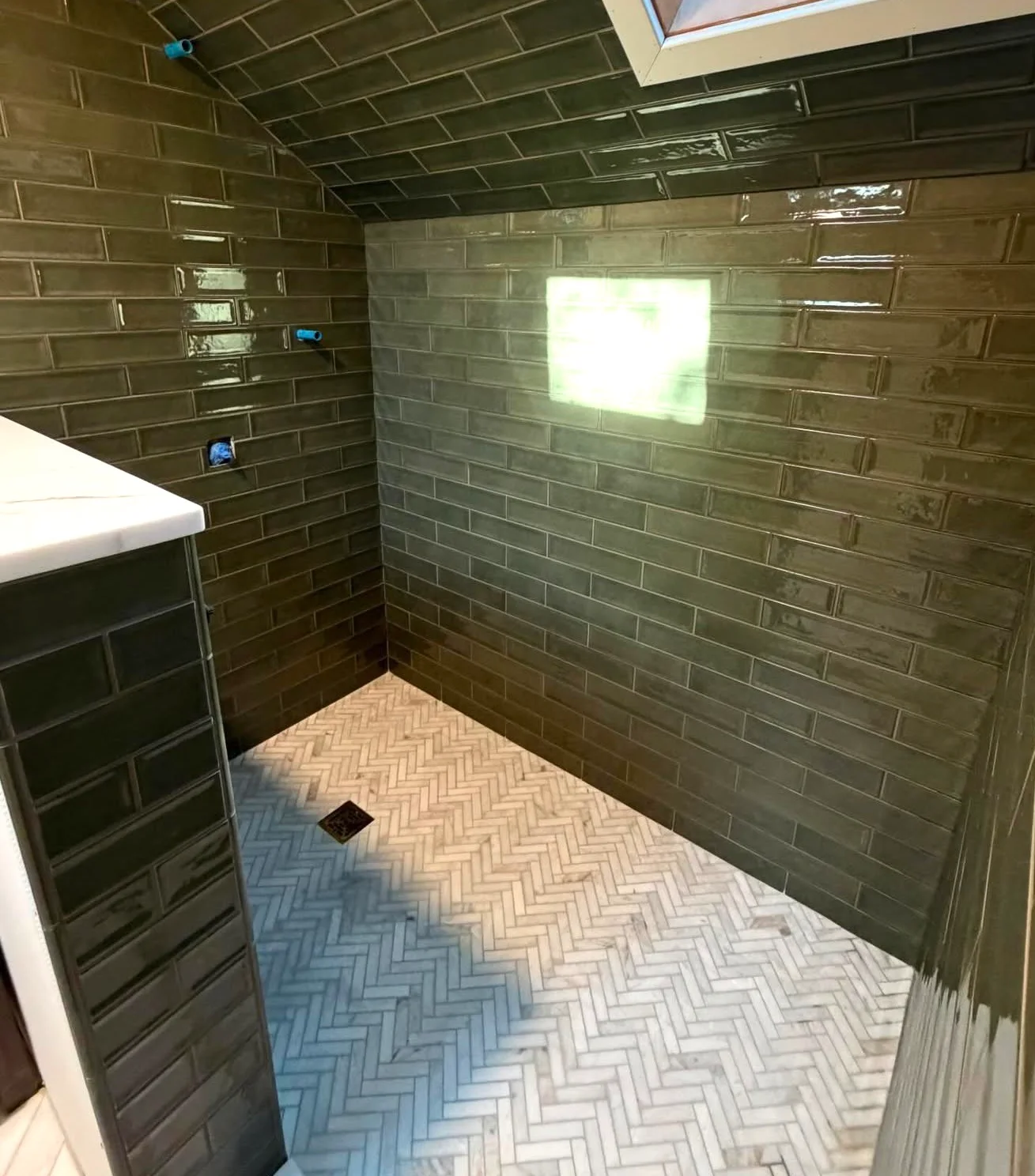 Dark green glazed wall tile paired with a light herringbone shower floor and square drain