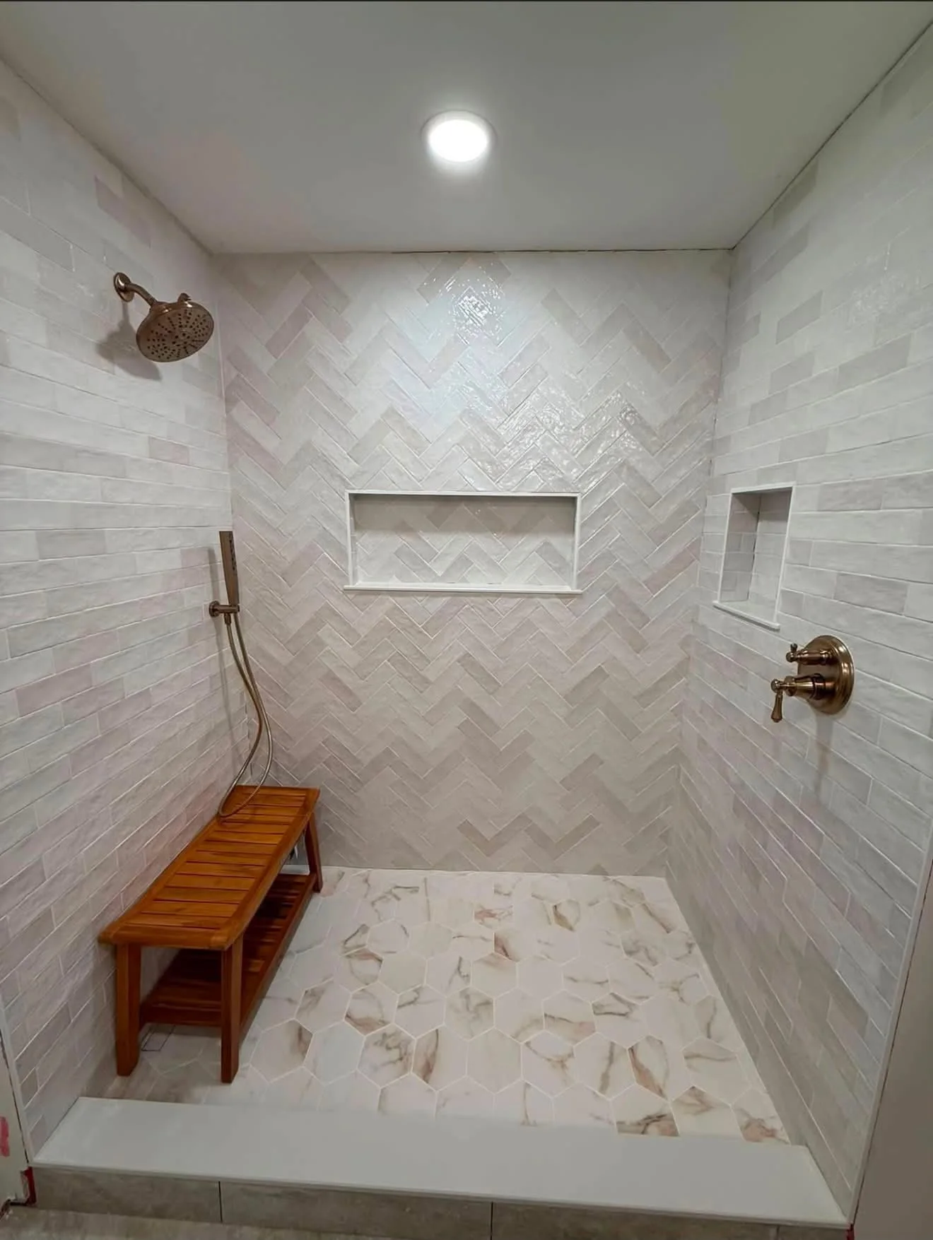Finished tiled walk-in shower with a herringbone feature wall, recessed niches, and hexagonal floor tile