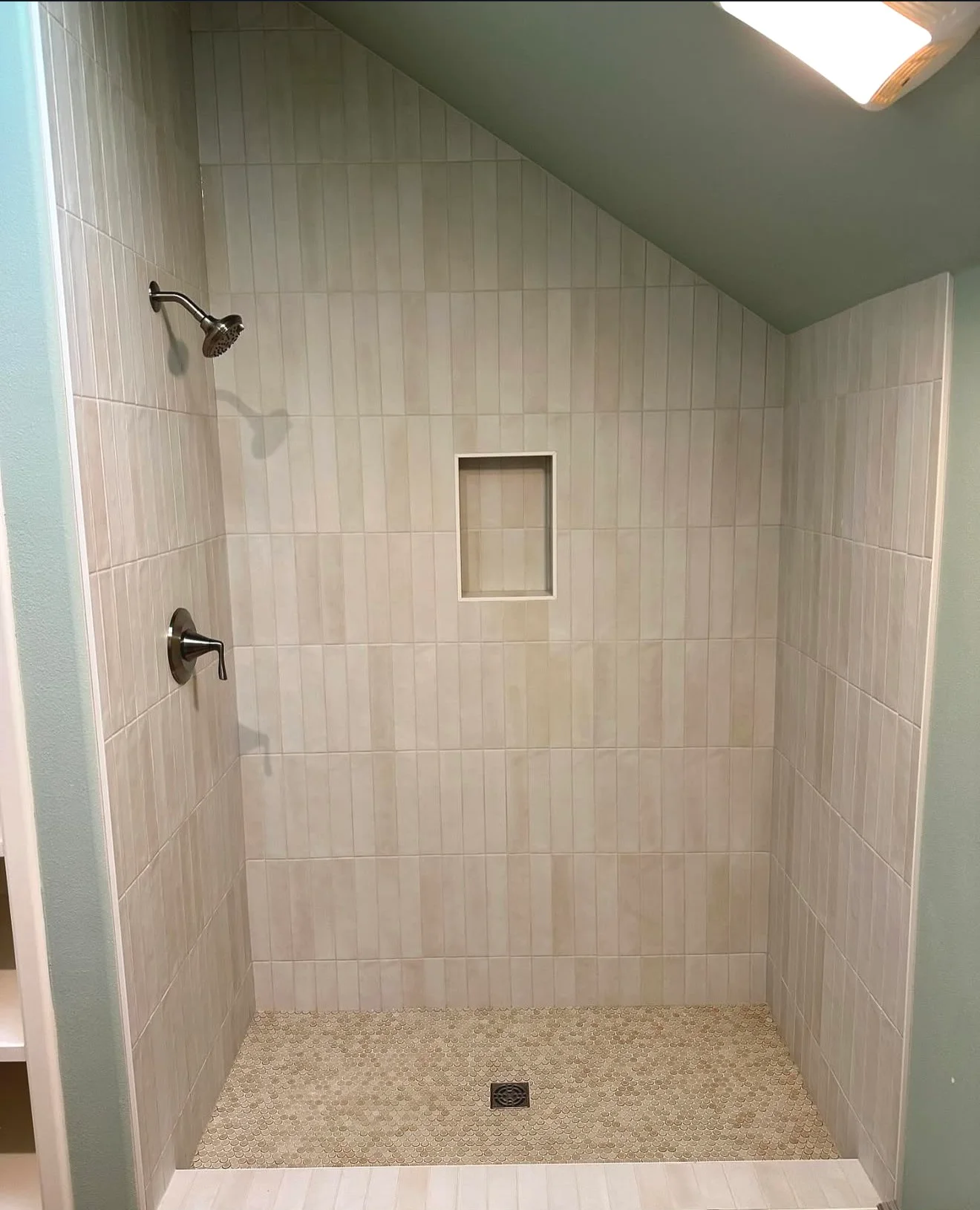 Finished white tile walk-in shower with recessed niche, mosaic floor, and square drain