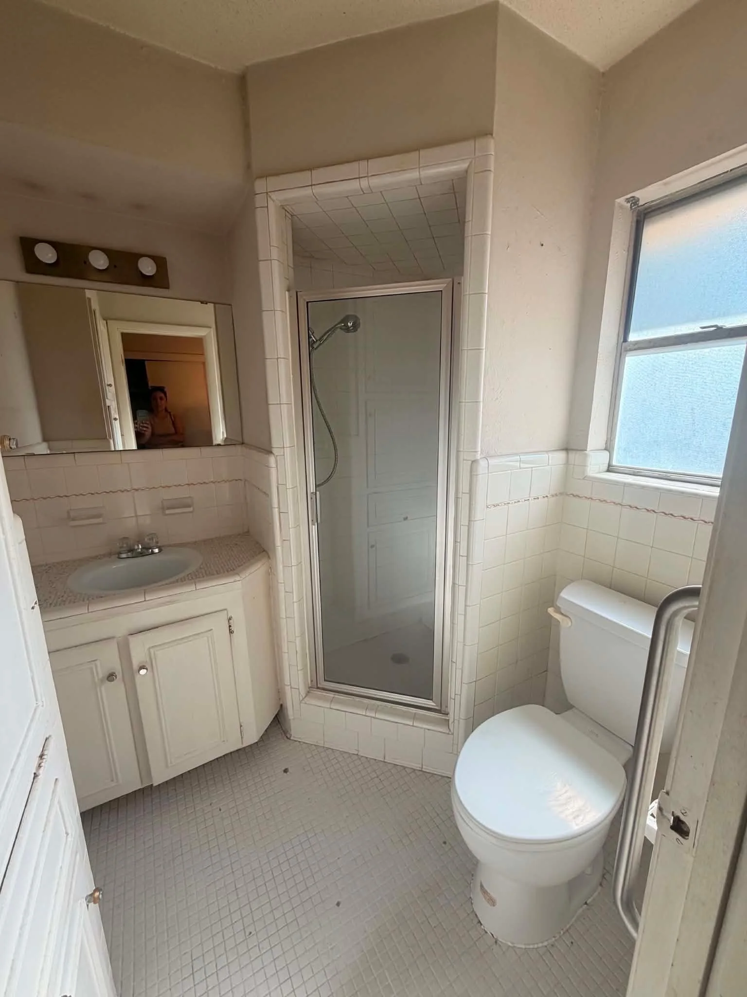 Compact existing bathroom with a shower, vanity, toilet, and window considered together during remodel planning