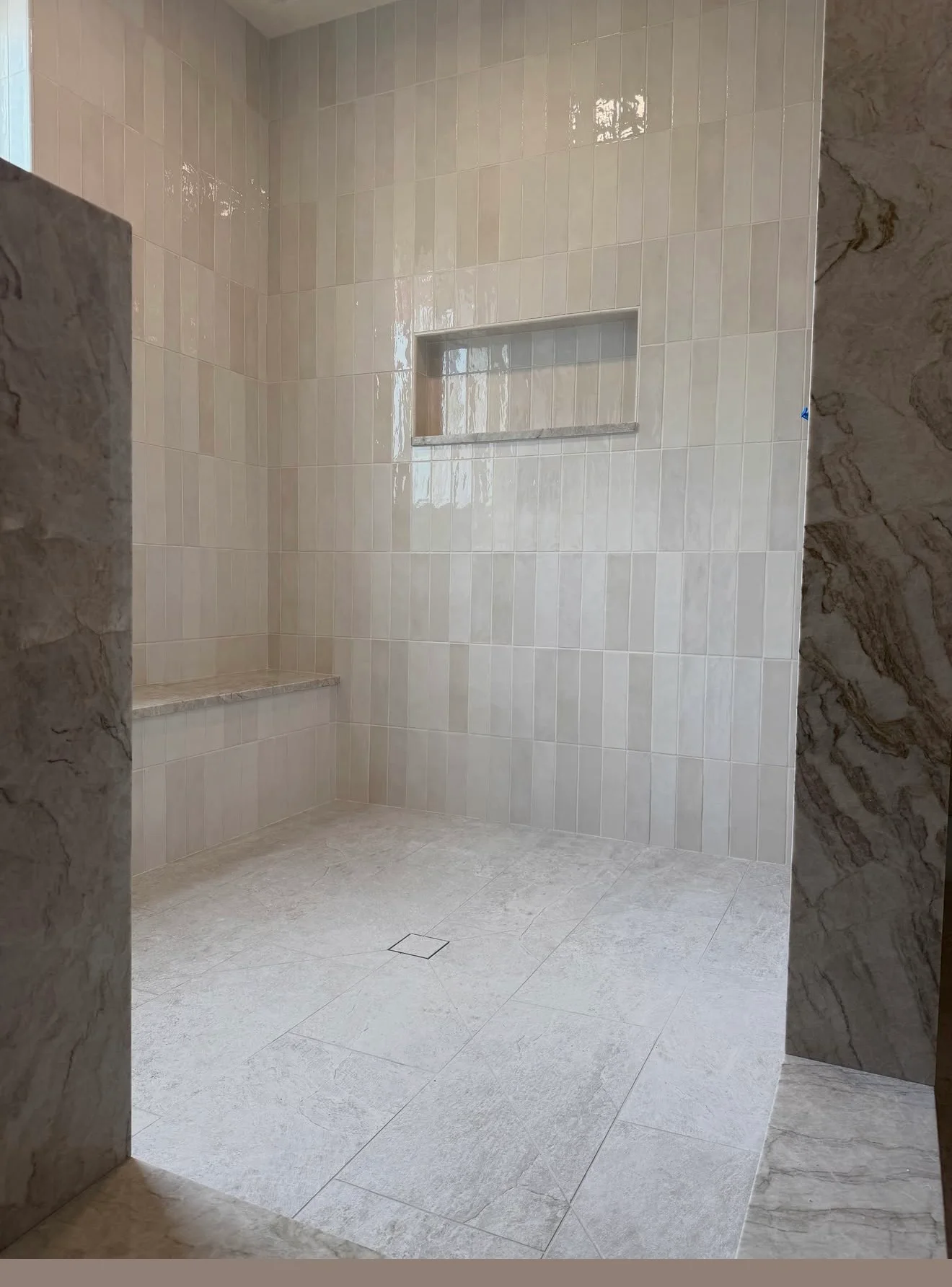 Tiled walk-in shower with a built-in bench, recessed niche, and large-format floor tile