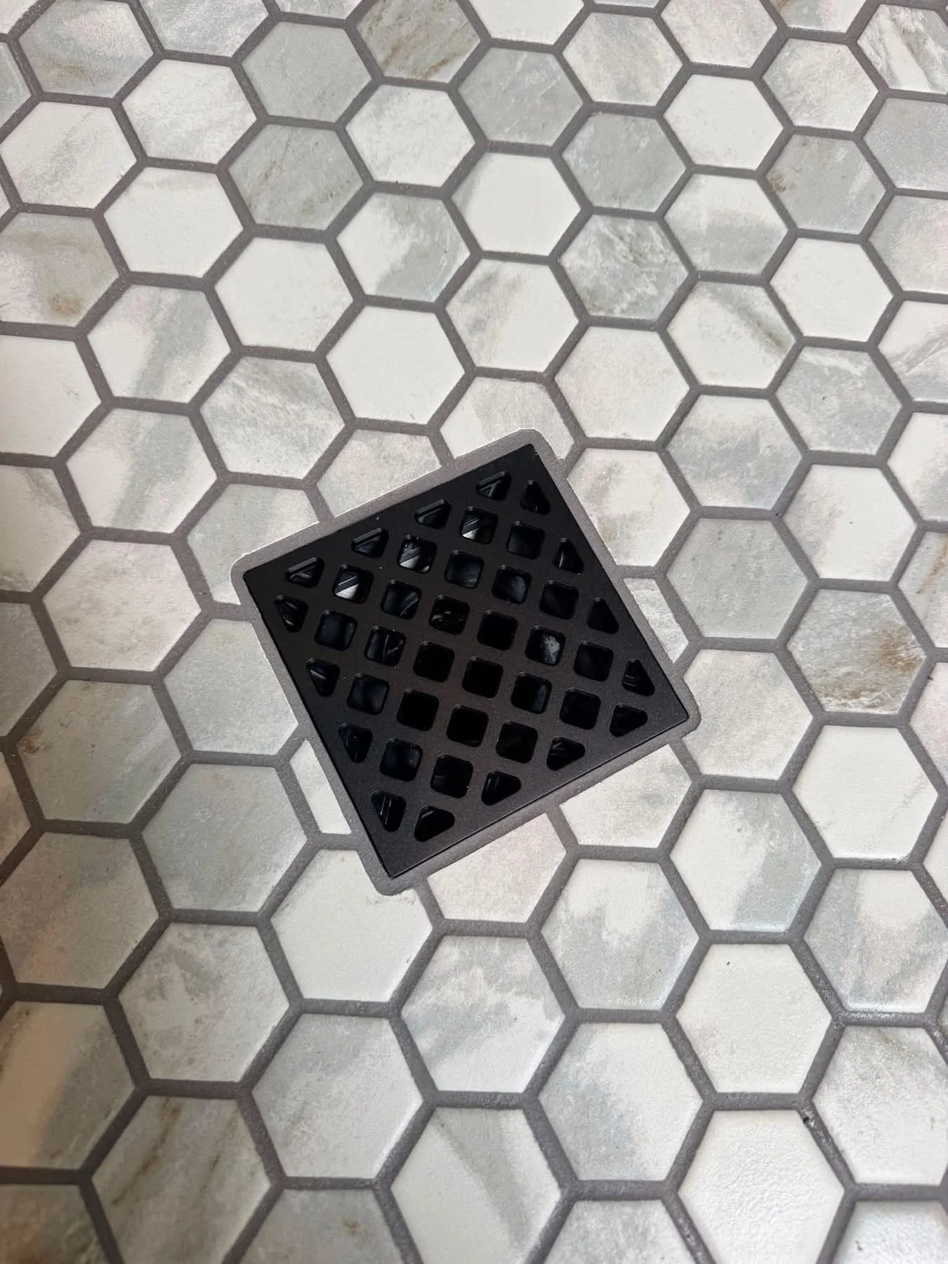 Hexagonal mosaic shower floor tile fitted around a square drain cover
