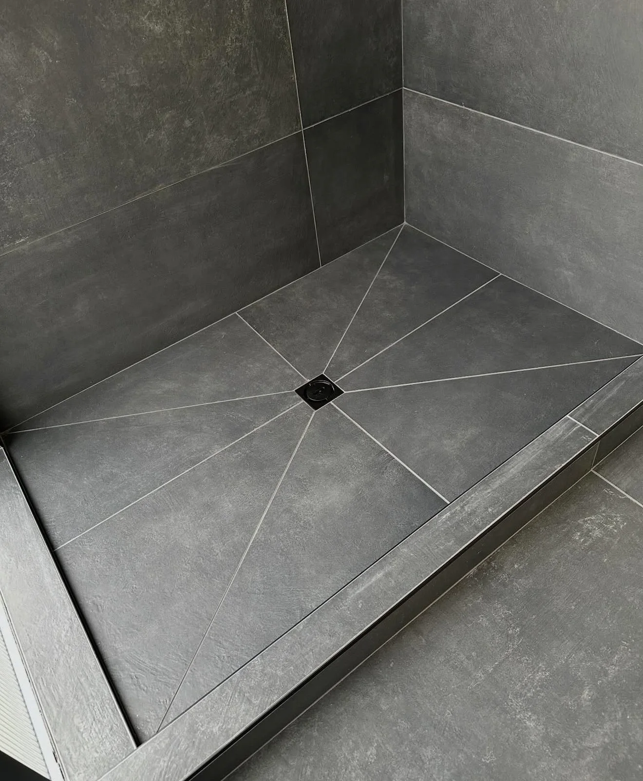 Dark large-format shower floor tile pitched toward a centered square drain