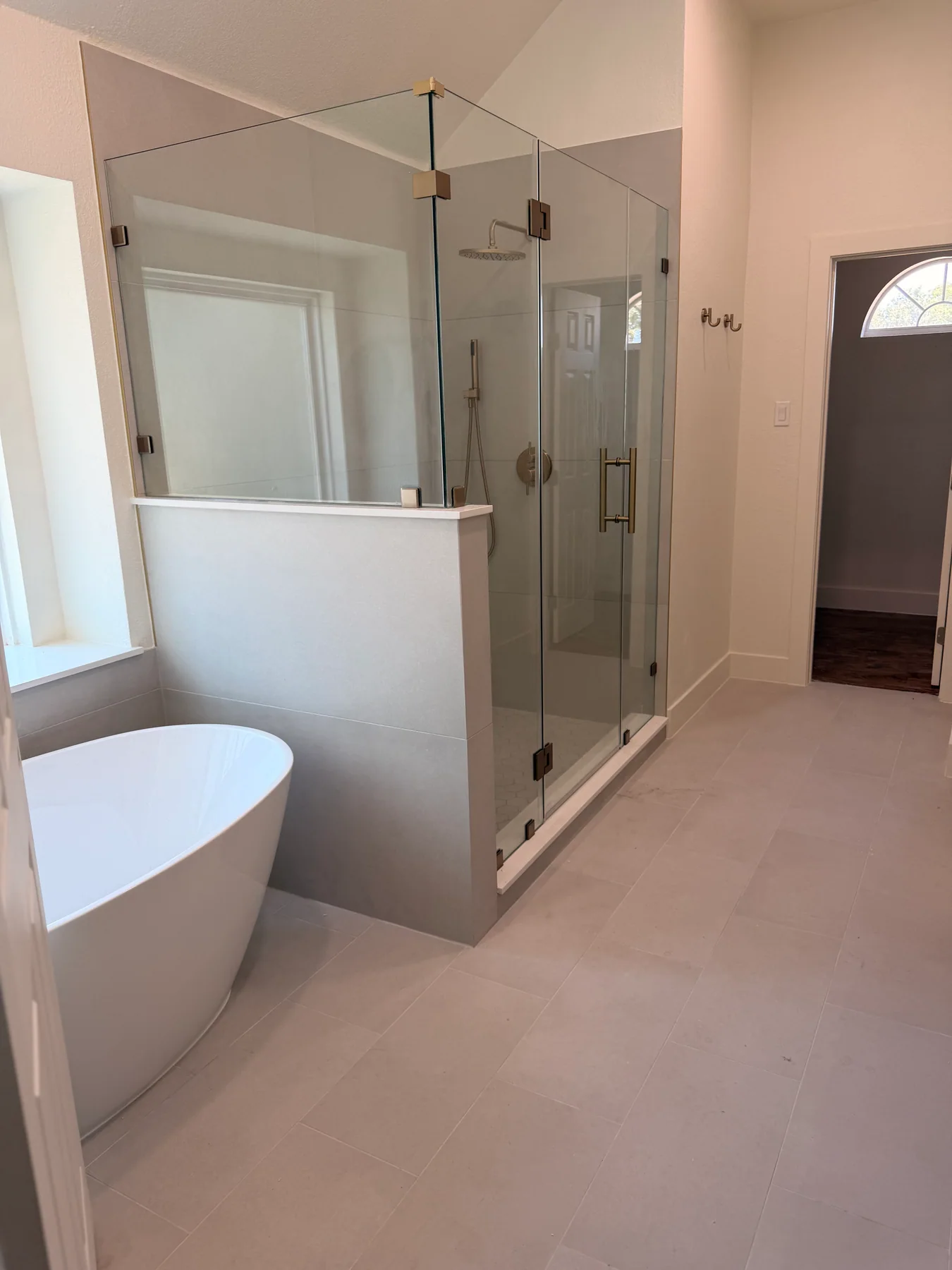 Freestanding bathtub beside a frameless glass shower with light tile and brass fixtures