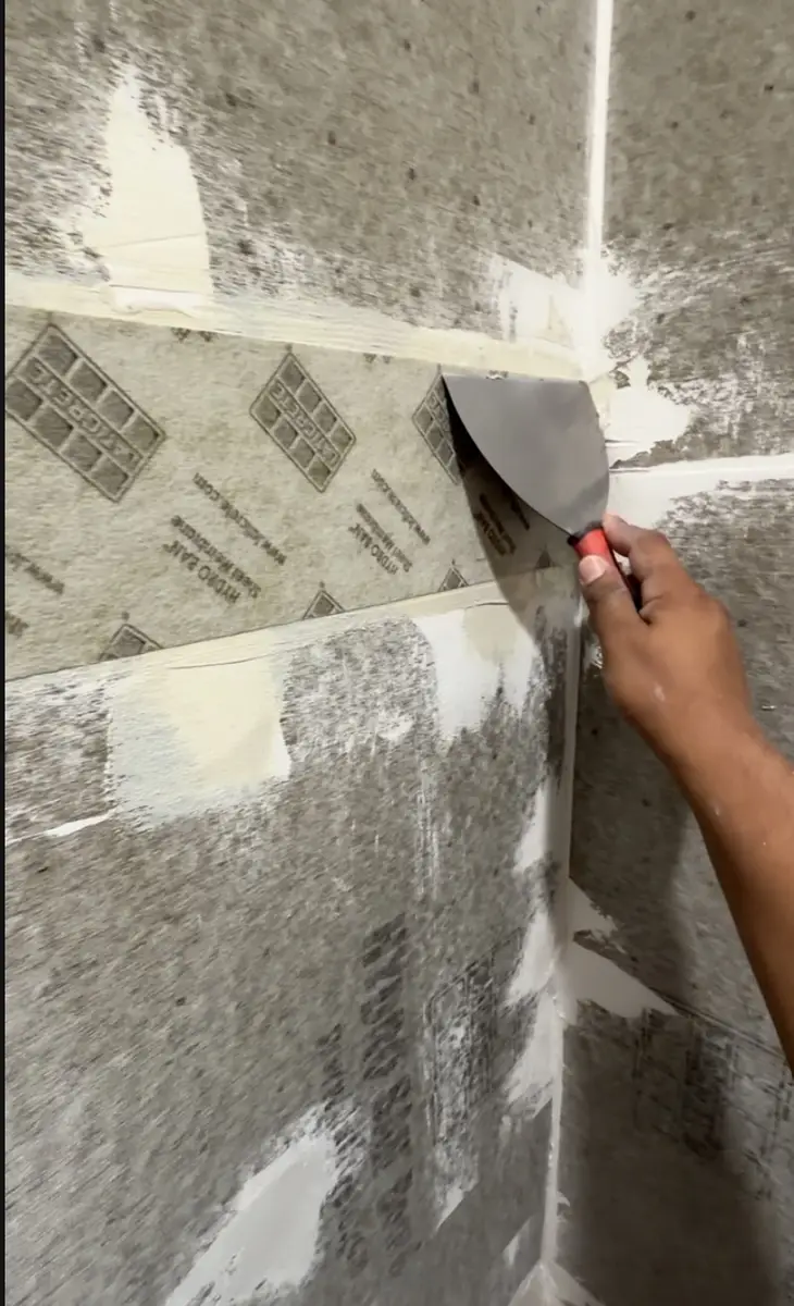 Applying HydroBan waterproofing membrane to shower walls with putty knife during bathroom remodel
