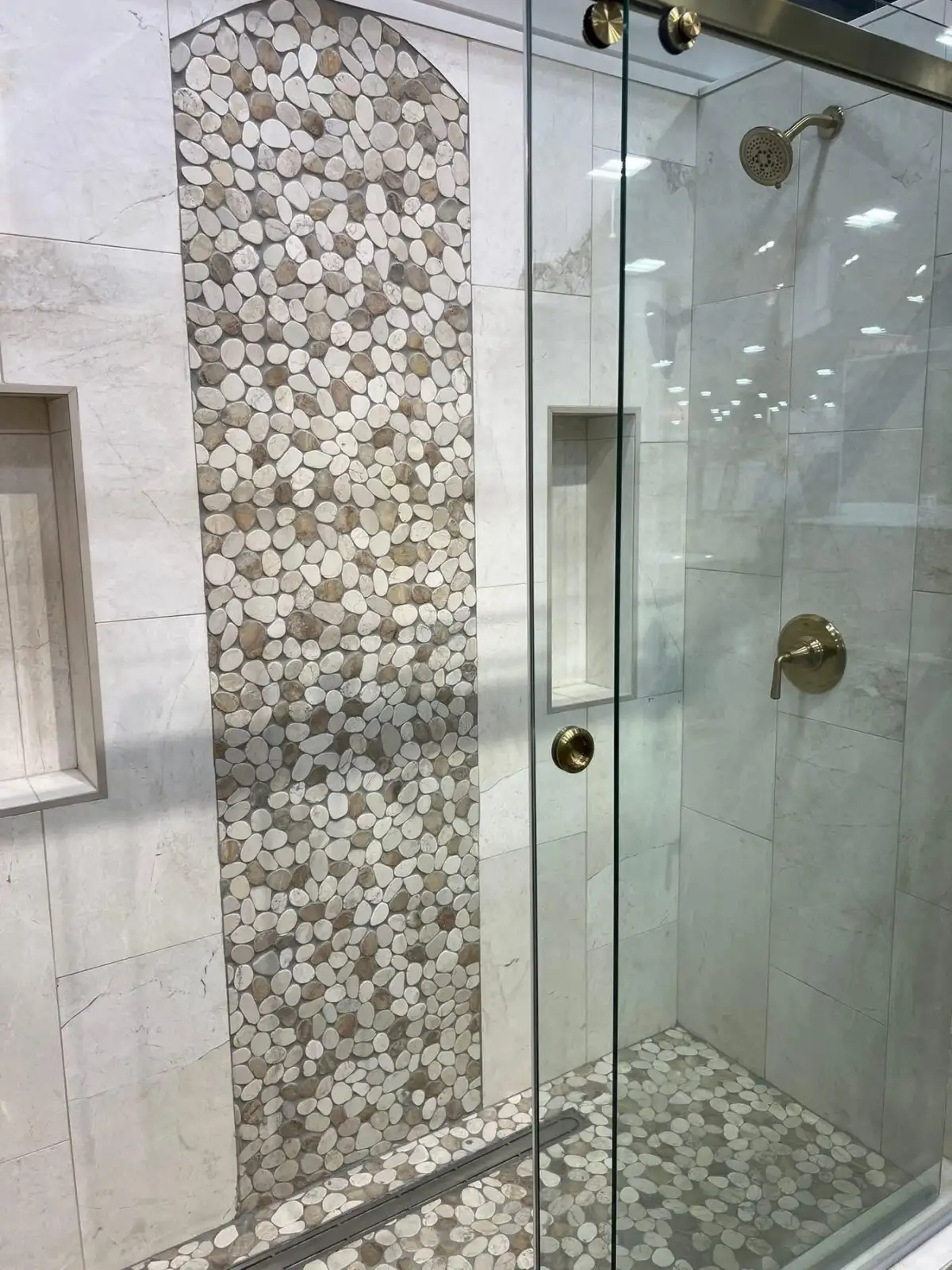 Marble walls with arched pebble accent, glass door, and gold hardware