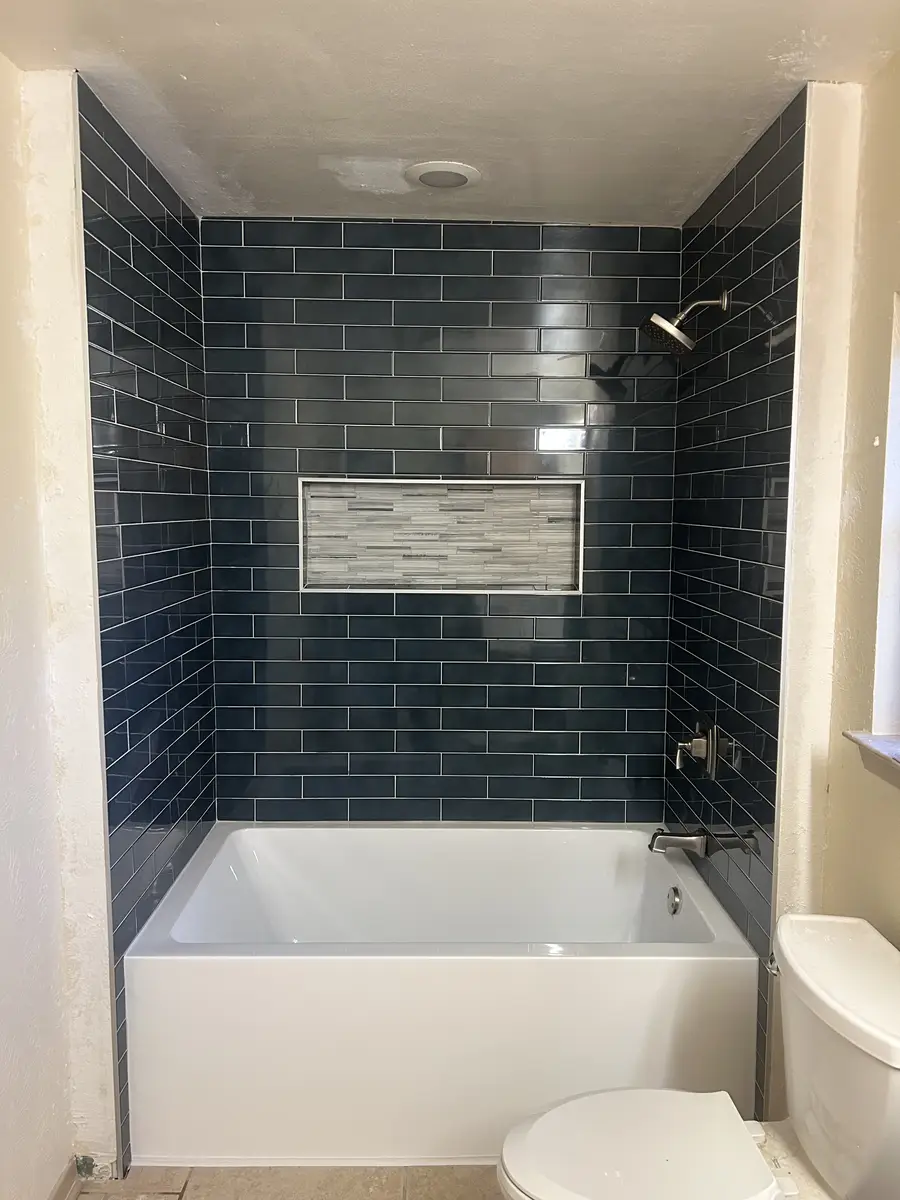 Tub-shower combo with dark blue subway tile surround, linear accent niche, and brushed nickel fixtures