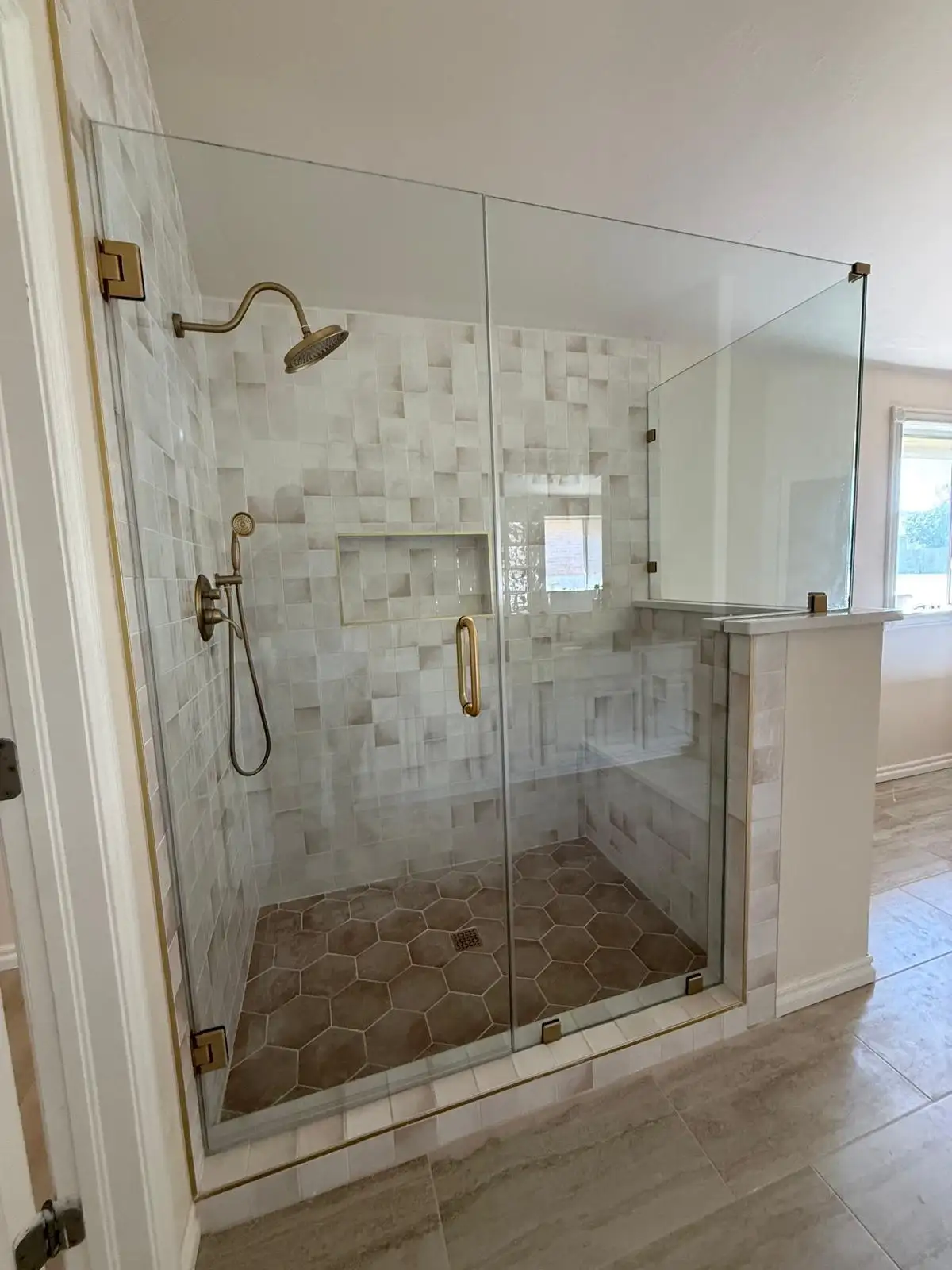 Large walk-in shower with zellige tile, frameless glass, gold fixtures, and hexagon floor